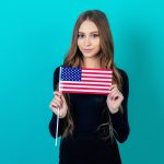 attractive female person holding an American flag in her hand on a blue background